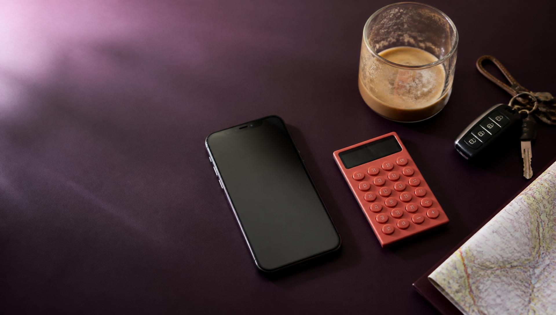 Modern flat lay of a phone, calculator, coffee and car keys on a deep purple desk